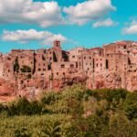 Idyllic medieval village perched on a cliff in Tuscany, Italy, under a bright blue sky.